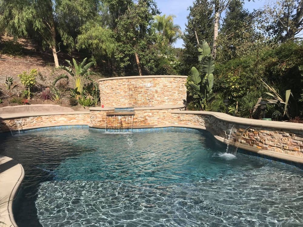 Luxurious backyard swimming pool with stone waterfall and lush tropical landscaping.